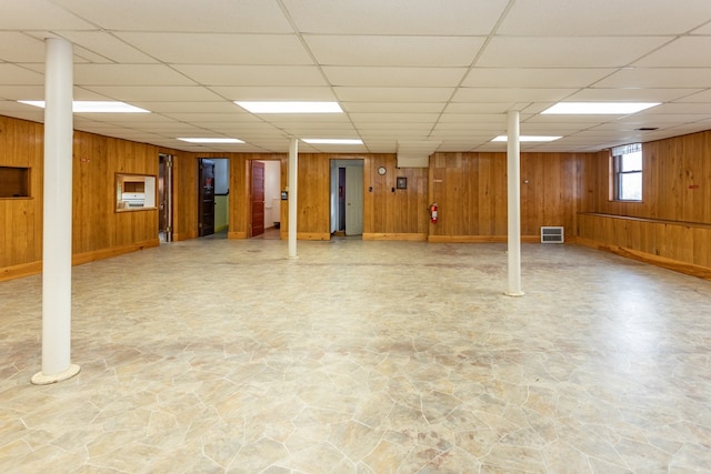 basement featuring visible vents, wood walls, and a paneled ceiling