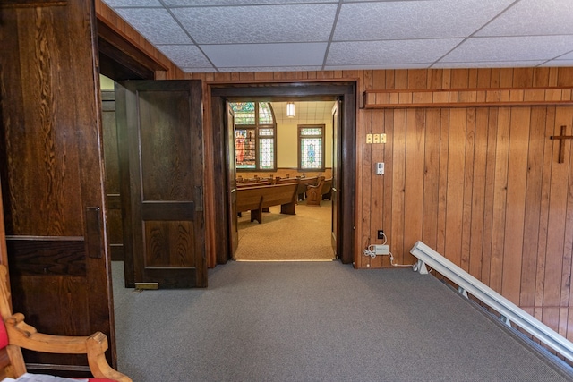 hall featuring carpet flooring, a paneled ceiling, and wooden walls