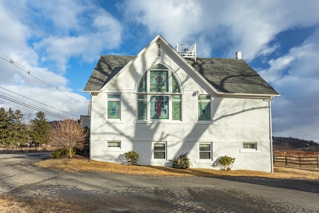 view of side of home with stucco siding, roof with shingles, and fence