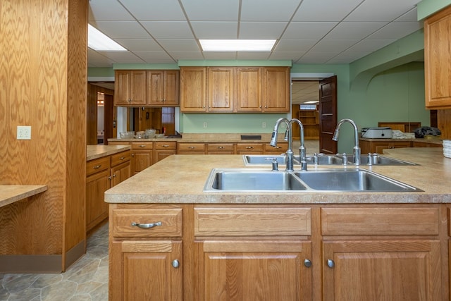 kitchen with a drop ceiling, stone finish flooring, light countertops, and a sink