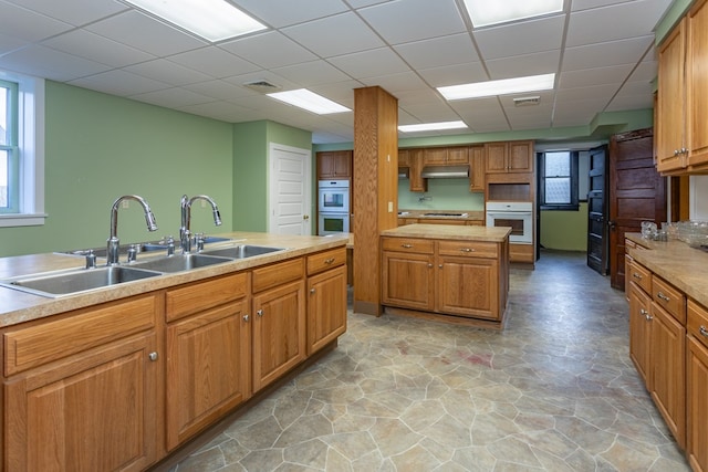 kitchen featuring under cabinet range hood, a paneled ceiling, a sink, and light countertops