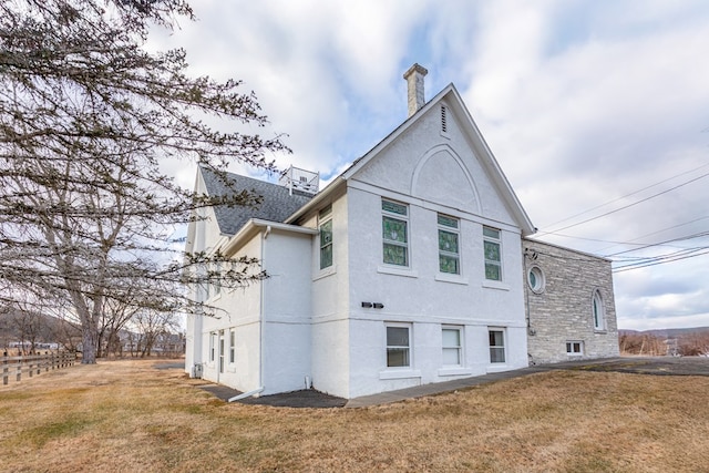 back of house with stucco siding, a chimney, and a yard