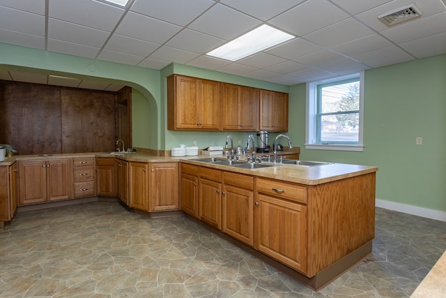 kitchen with visible vents, a peninsula, a sink, light countertops, and a paneled ceiling