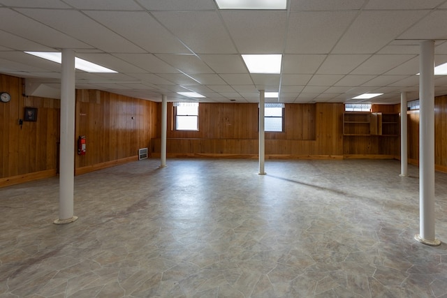 below grade area with wooden walls, a paneled ceiling, and visible vents