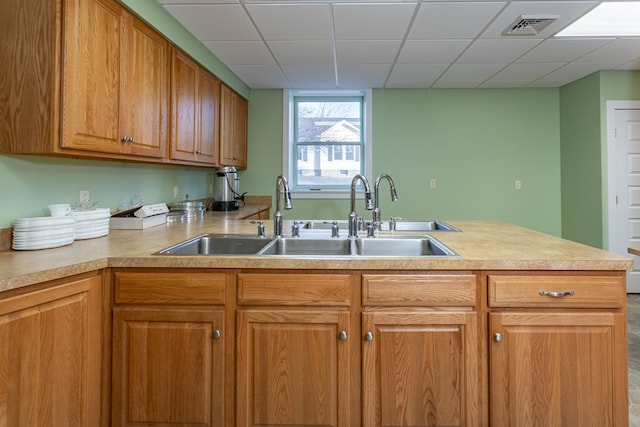 kitchen with visible vents, brown cabinets, a sink, a peninsula, and light countertops