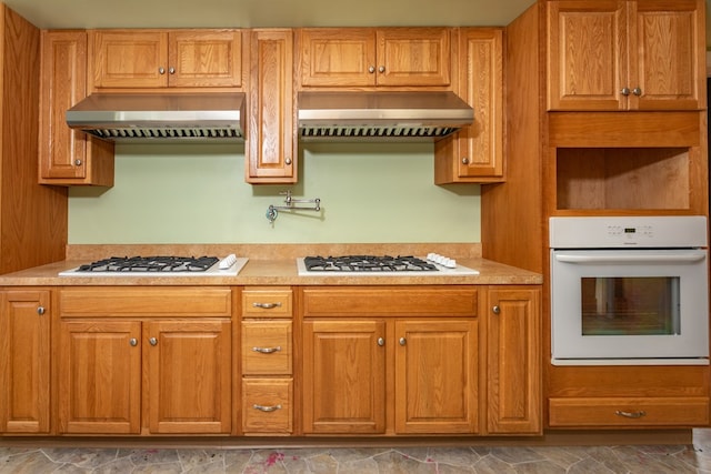 kitchen featuring white appliances, extractor fan, under cabinet range hood, and light countertops