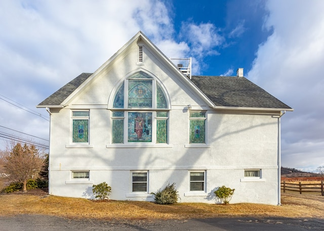 view of side of property with a shingled roof, fence, and stucco siding