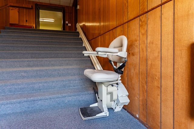 stairway with a paneled ceiling, carpet floors, and wood walls