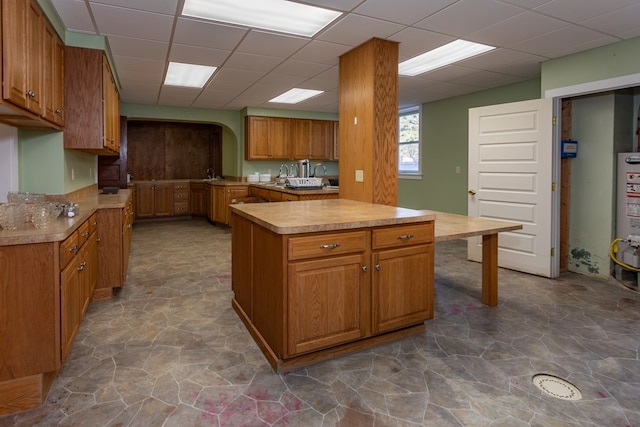 kitchen featuring stone finish floor, arched walkways, brown cabinetry, light countertops, and a paneled ceiling