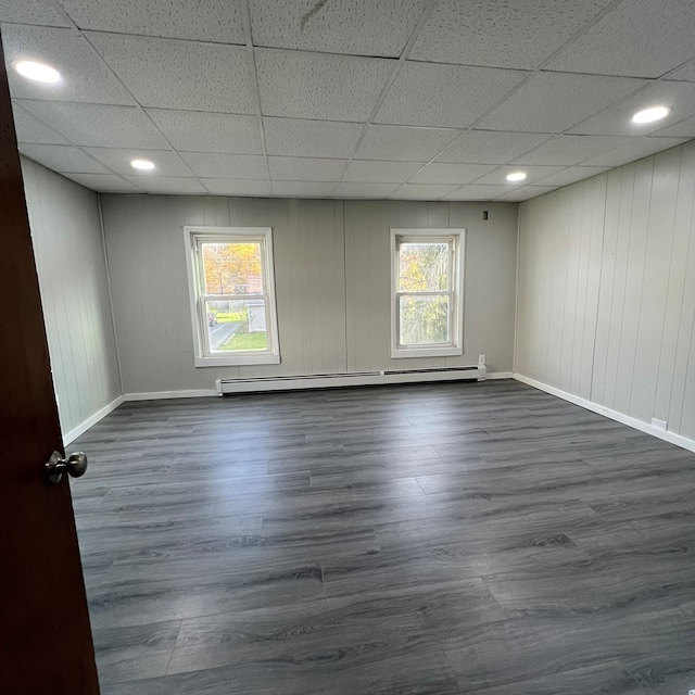 empty room with a wealth of natural light, a paneled ceiling, dark hardwood / wood-style floors, and baseboard heating