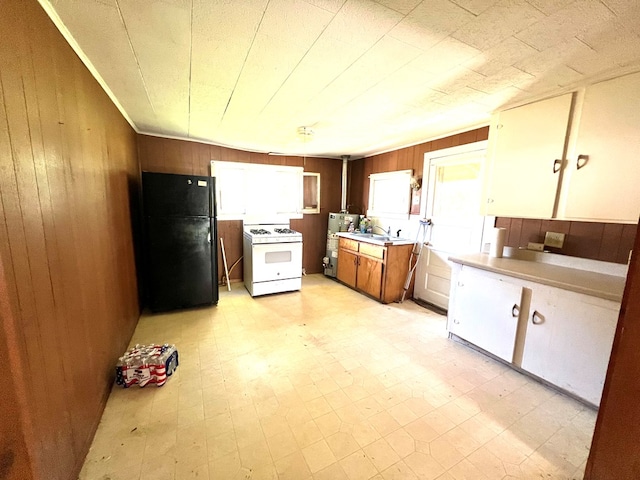 kitchen with black fridge, white gas range, sink, white cabinets, and wood walls