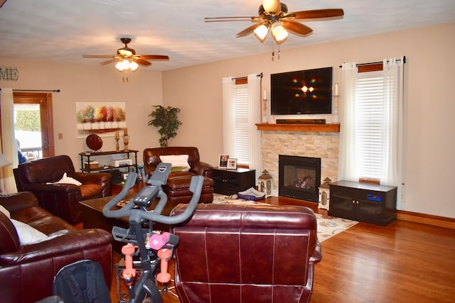 living room featuring hardwood / wood-style flooring, a stone fireplace, and ceiling fan