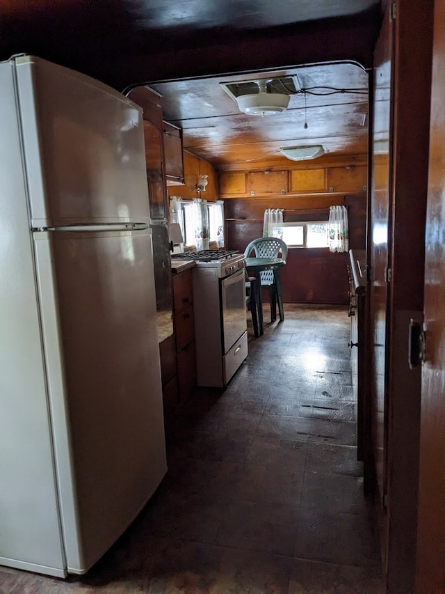 kitchen with white range with gas stovetop, refrigerator, and wooden walls