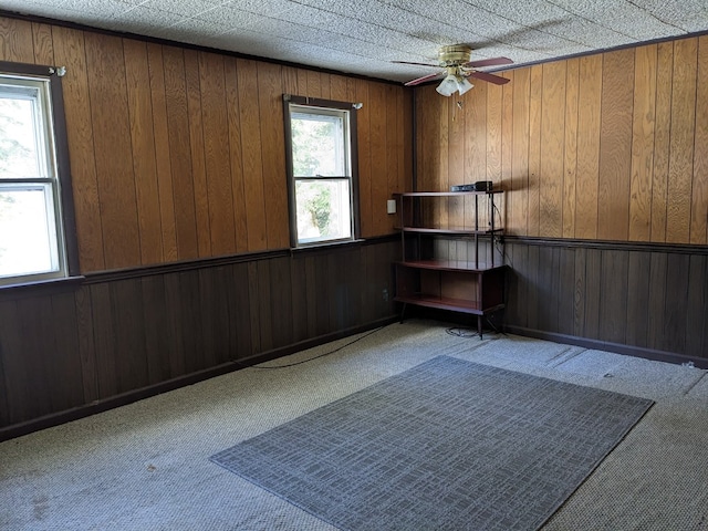 empty room with ceiling fan, a healthy amount of sunlight, wood walls, and light carpet