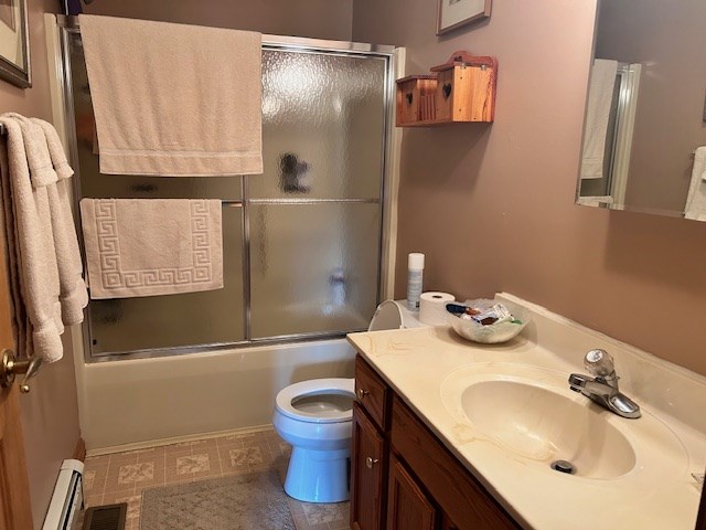 full bathroom featuring toilet, vanity, a baseboard heating unit, and combined bath / shower with glass door