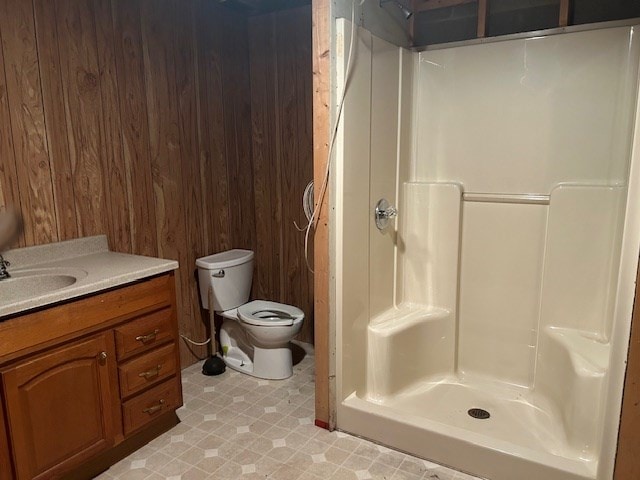 bathroom with vanity, wood walls, toilet, and walk in shower