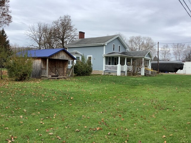 back of property featuring covered porch, a yard, and a shed