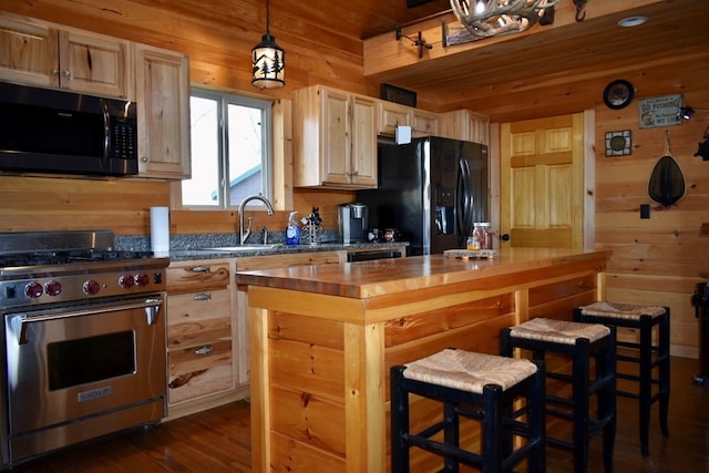 kitchen with wood walls, hanging light fixtures, light brown cabinetry, appliances with stainless steel finishes, and butcher block countertops