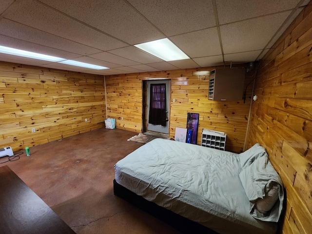 bedroom with a paneled ceiling, concrete floors, and wood walls