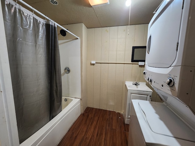 bathroom with stacked washer and clothes dryer, sink, wood walls, wood-type flooring, and shower / bath combo