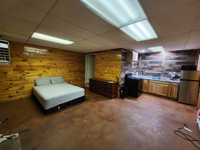 unfurnished bedroom with wooden walls, stainless steel fridge, concrete flooring, and a drop ceiling