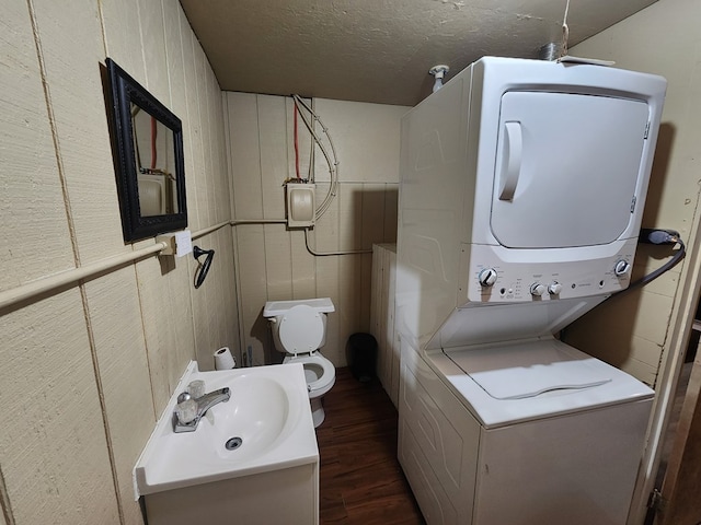 bathroom with toilet, a textured ceiling, vanity, stacked washing maching and dryer, and hardwood / wood-style floors