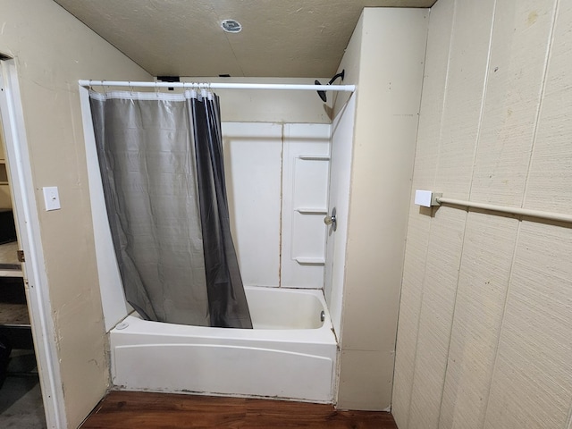 bathroom with wood-type flooring, shower / tub combo with curtain, and a textured ceiling