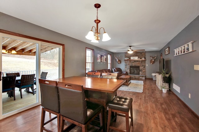 dining room featuring ceiling fan with notable chandelier, hardwood / wood-style flooring, and a stone fireplace