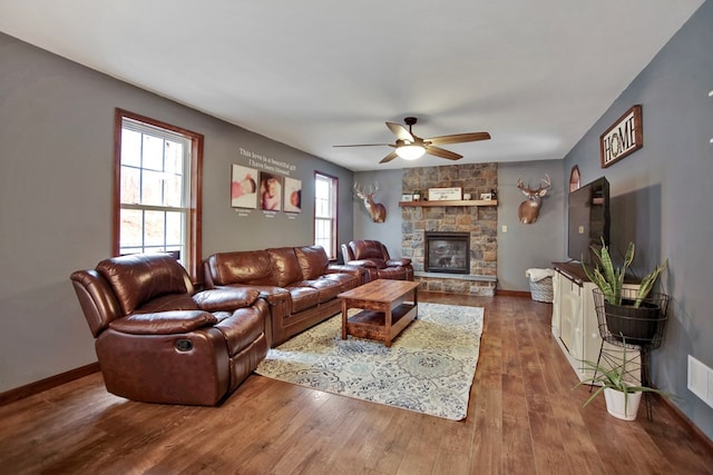 living room featuring ceiling fan, hardwood / wood-style floors, and a stone fireplace