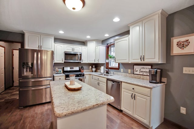 kitchen with stainless steel appliances, a kitchen island, light stone countertops, sink, and wood-type flooring