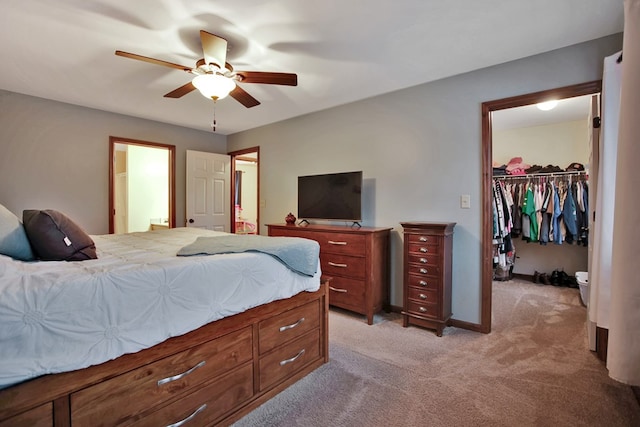 bedroom with connected bathroom, light colored carpet, a walk in closet, a closet, and ceiling fan