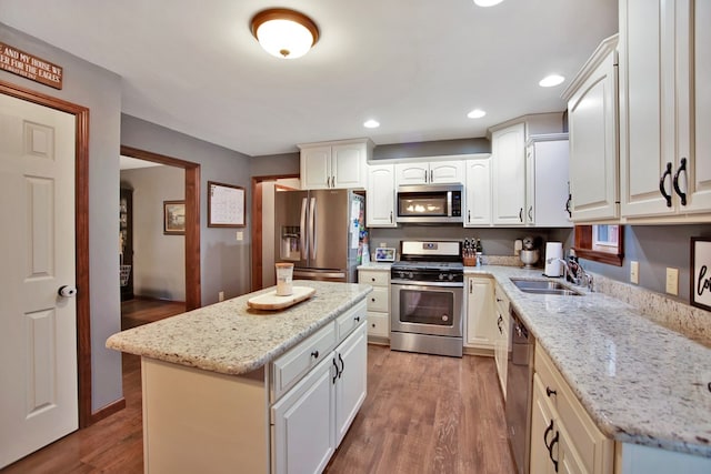 kitchen with appliances with stainless steel finishes, light stone counters, white cabinets, a kitchen island, and sink