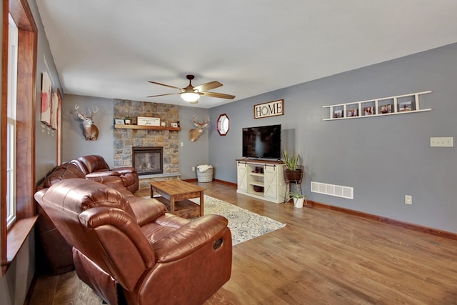 living room featuring light hardwood / wood-style floors, ceiling fan, and a stone fireplace