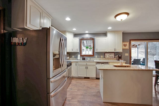 kitchen featuring stainless steel appliances, light stone countertops, light hardwood / wood-style floors, sink, and white cabinets