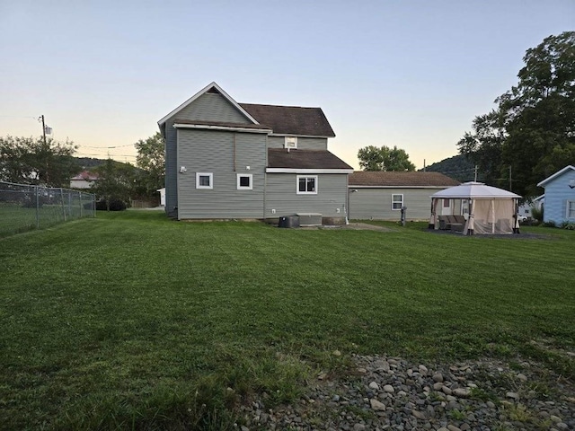 back house at dusk with a gazebo, central AC unit, and a yard