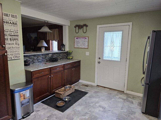 kitchen with pendant lighting, dark brown cabinets, light stone counters, and stainless steel refrigerator