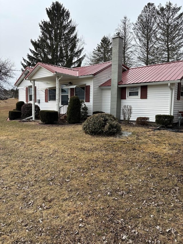 back of property with metal roof, a yard, a chimney, and a porch