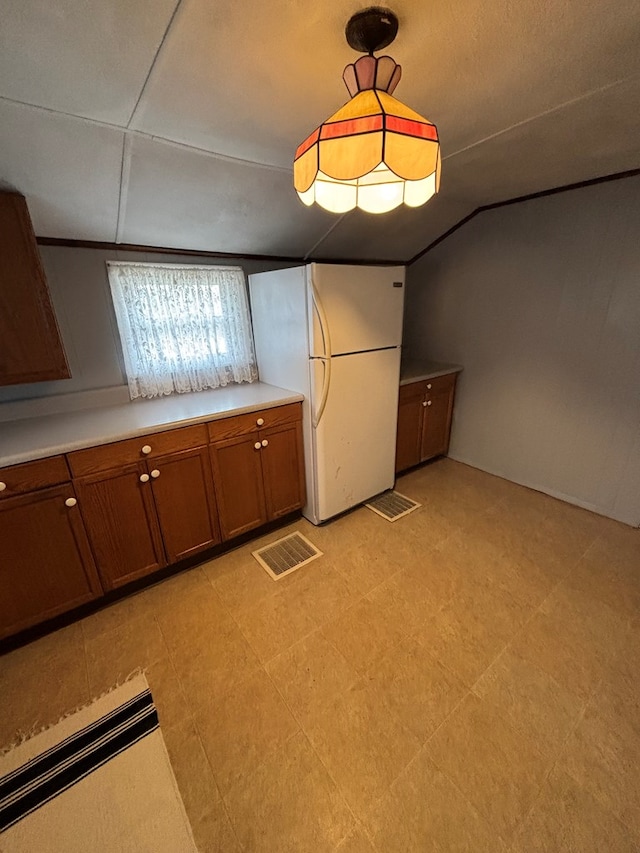 kitchen with lofted ceiling, visible vents, light countertops, freestanding refrigerator, and brown cabinets