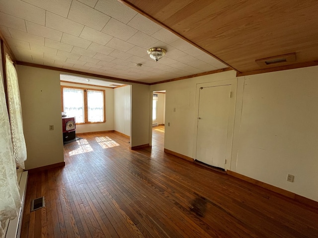 unfurnished bedroom with a wood stove, wood-type flooring, a baseboard heating unit, and ornamental molding