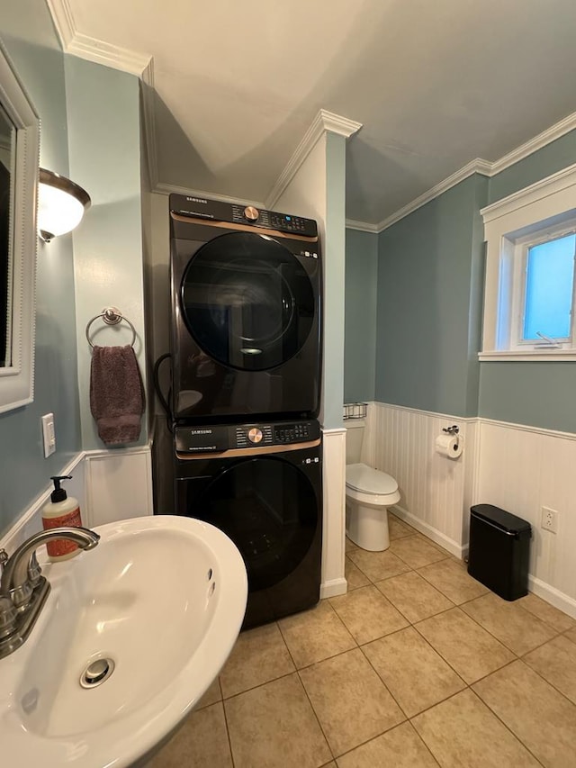 half bathroom featuring stacked washer and dryer, ornamental molding, a sink, and a wainscoted wall