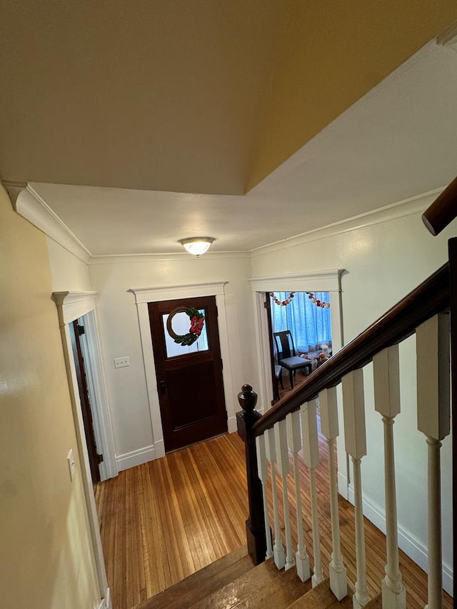 entryway featuring decorative columns, ornamental molding, wood finished floors, baseboards, and stairs