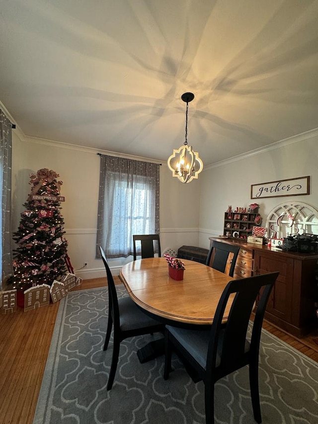 dining space featuring ornamental molding, a wainscoted wall, an inviting chandelier, and wood finished floors