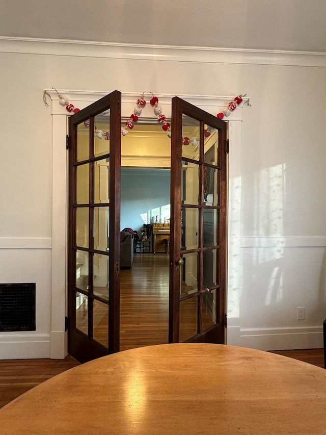 interior space with visible vents, wood finished floors, crown molding, french doors, and a fireplace