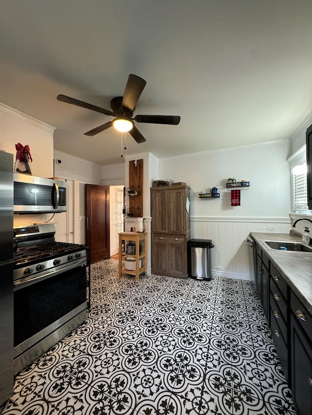 kitchen with appliances with stainless steel finishes, wainscoting, a sink, and ornamental molding