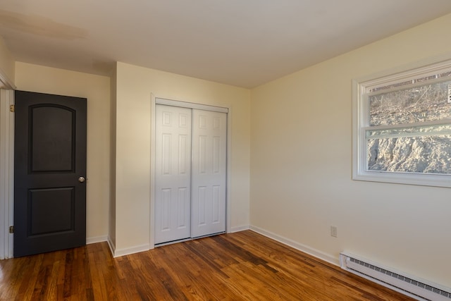 unfurnished bedroom with dark hardwood / wood-style flooring, baseboard heating, and a closet