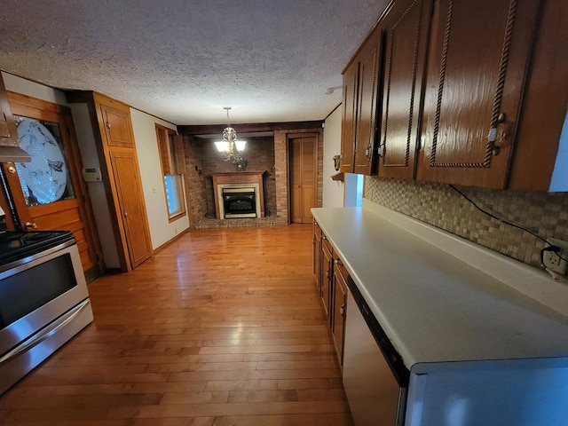 kitchen featuring decorative backsplash, a brick fireplace, a textured ceiling, range, and light hardwood / wood-style floors