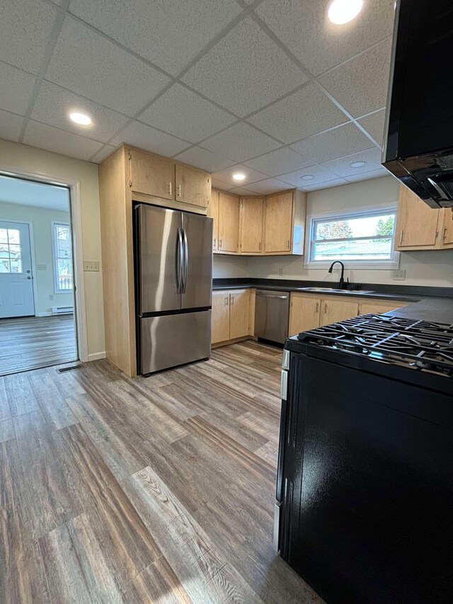 kitchen featuring light brown cabinetry, light wood-type flooring, stainless steel appliances, and a drop ceiling