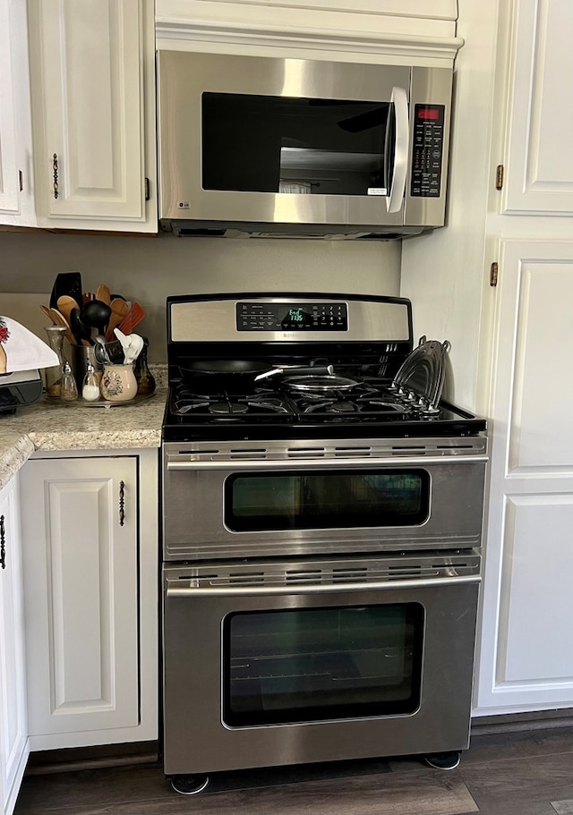 kitchen with stainless steel appliances, white cabinetry, dark wood-type flooring, and light stone counters