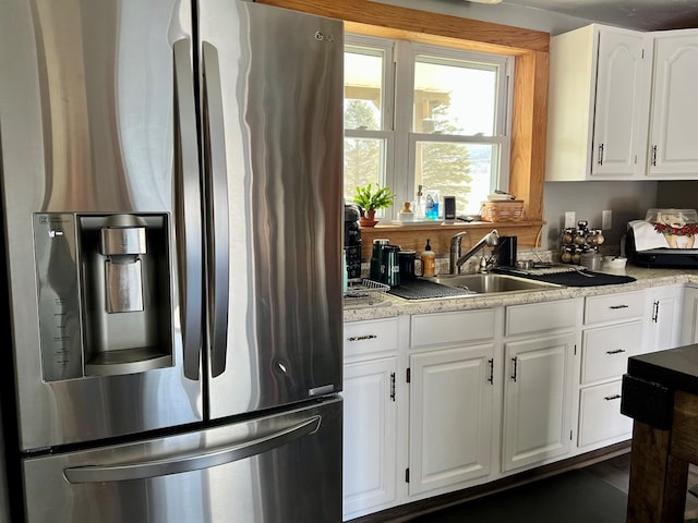 kitchen with stainless steel fridge, white cabinetry, and sink