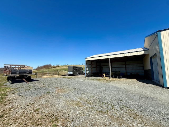 garage featuring a carport, gravel driveway, a rural view, and fence